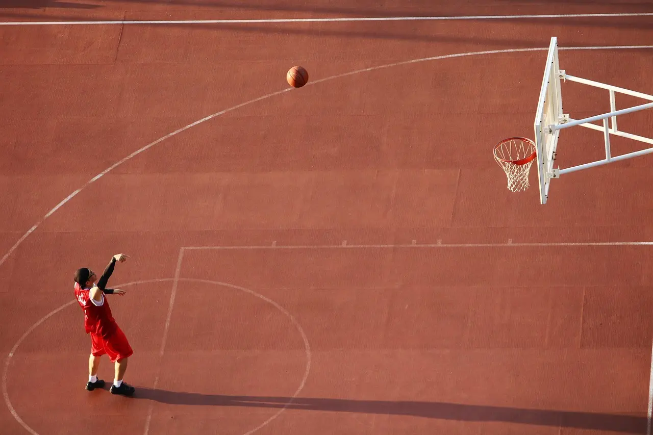 Basketballspiller i rød dragt skyder mod kurv