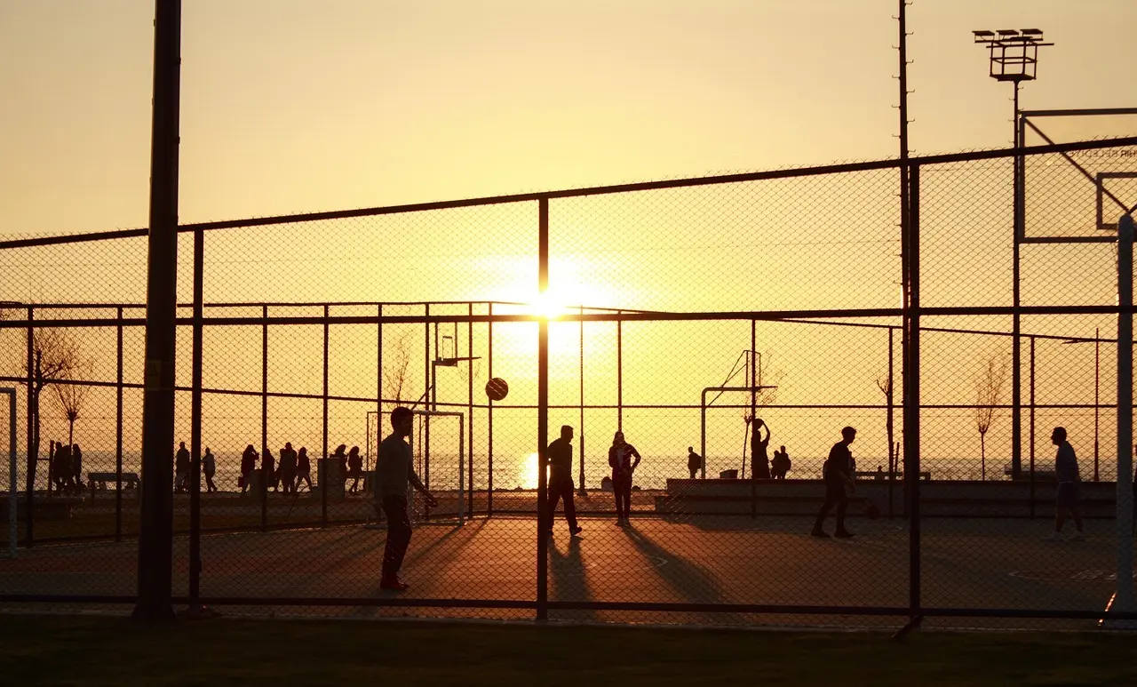 Udendørs basketballbane med spillere i silhuet ved solnedgang
